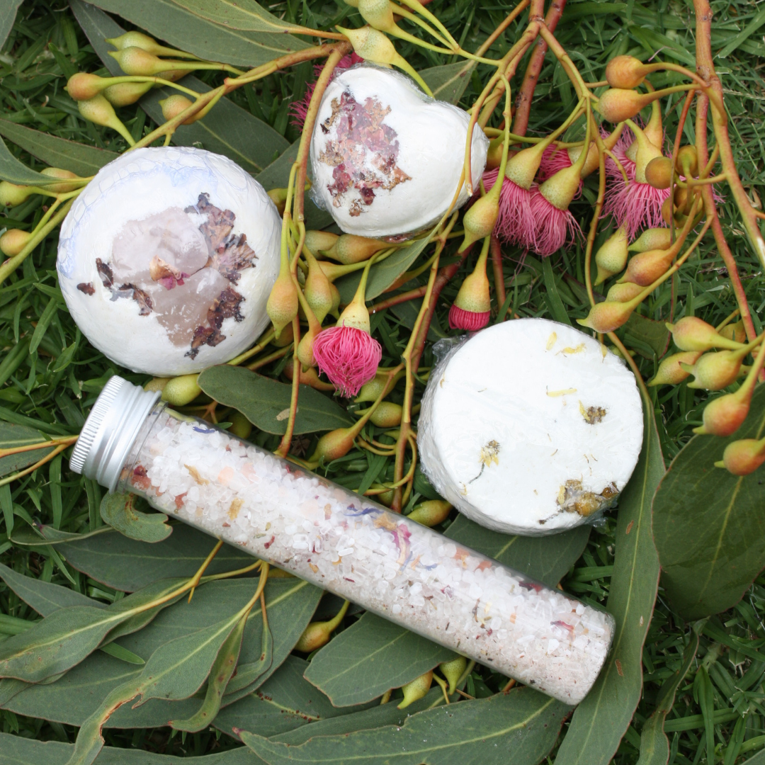 Bath bombs and a tube of bath salts on eucalyptus leaves with pink flowers.