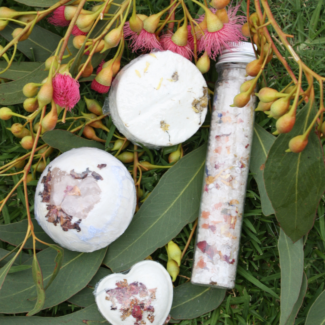 Bath bombs and a tube of bath salts on green leaves with pink flowers