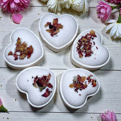 Heart-shaped bath bombs with dried flowers on a wooden surface with flowers around
